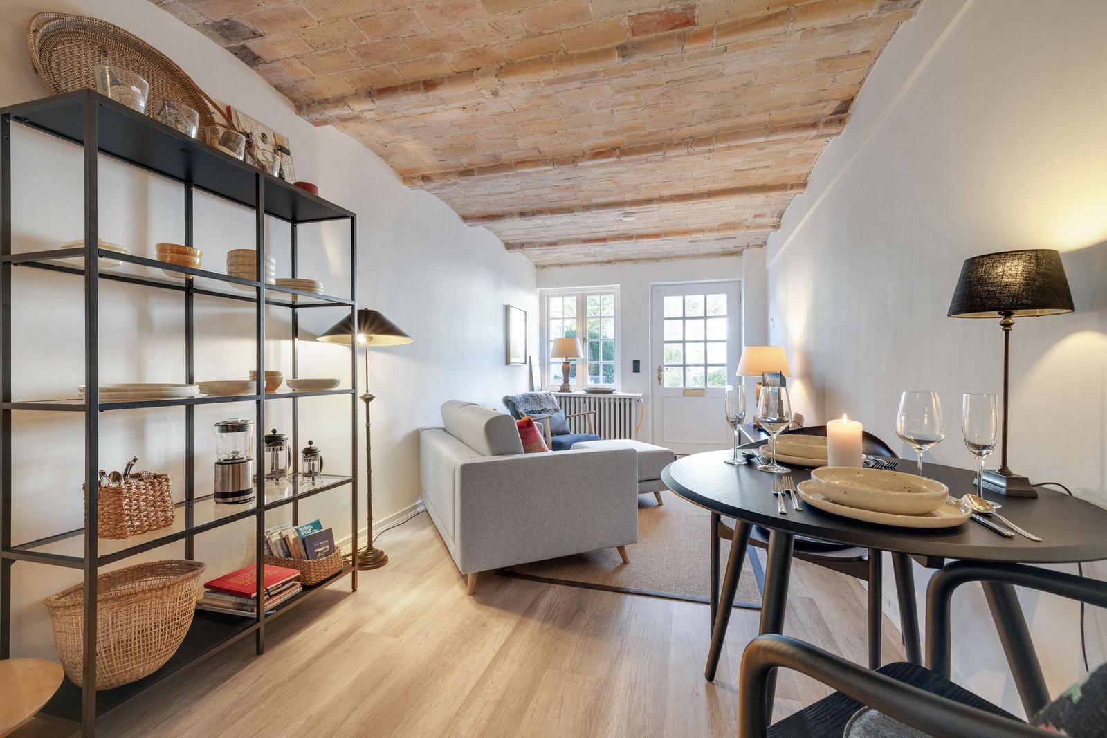 Living and dining area with wooden floor, table, and sofa under beam ceiling.