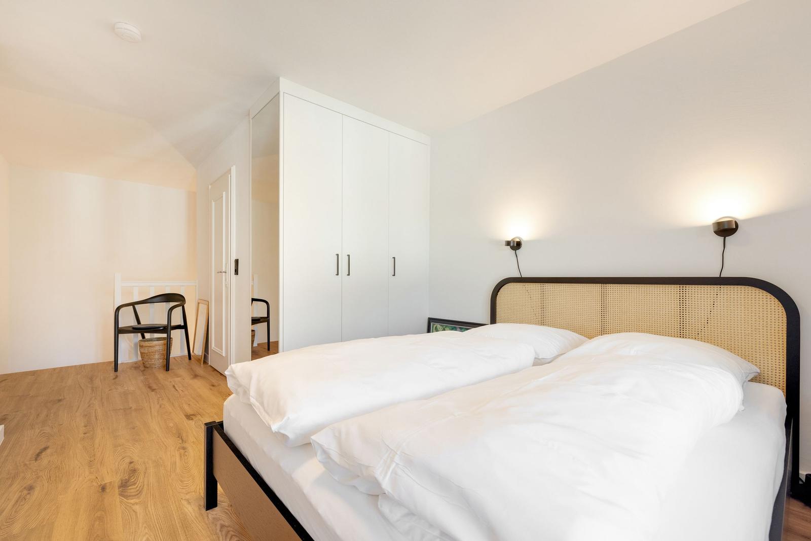 Bedroom with double bed, white walls, and wooden floor. Two wall lamps are mounted.