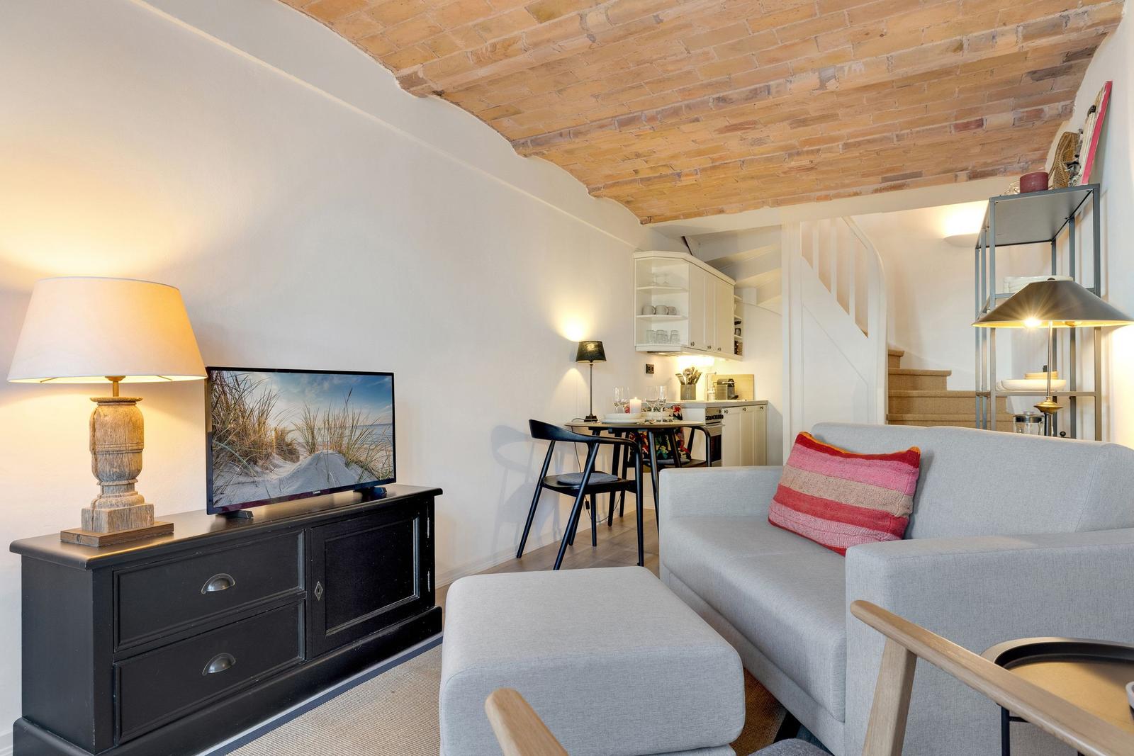 Living room with sofa, TV, and dining area under brick ceiling.