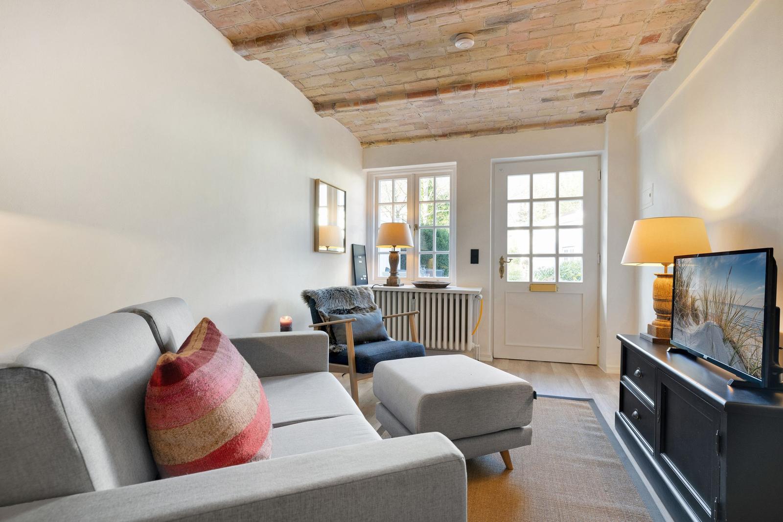 Living room with sofa, armchair, and TV under wooden beam ceiling.