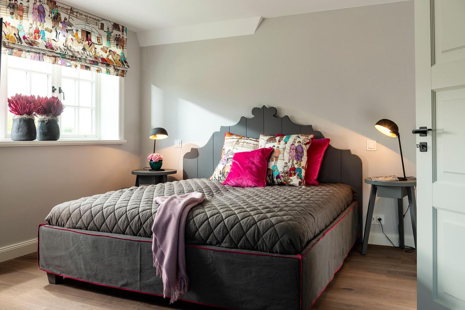 Schlafzimmer mit Bett, Nachttischen und Fenster mit Vorhang.