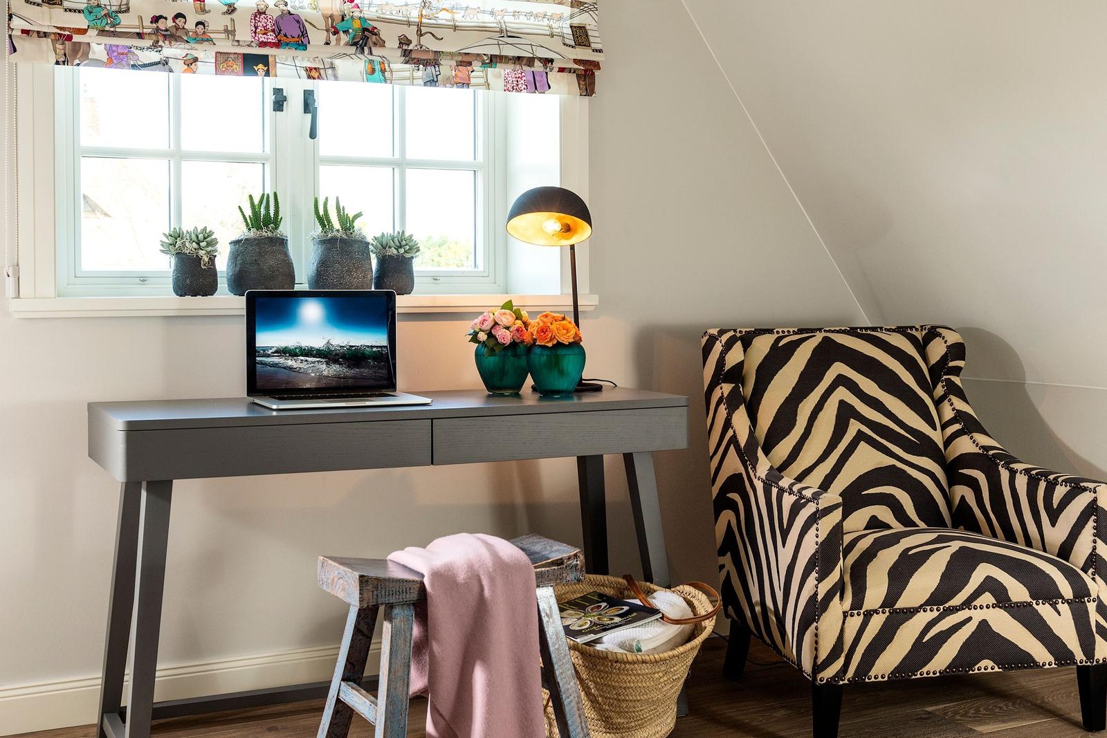 Schreibtisch mit Laptop, Stuhl und Blumen unter Fenster