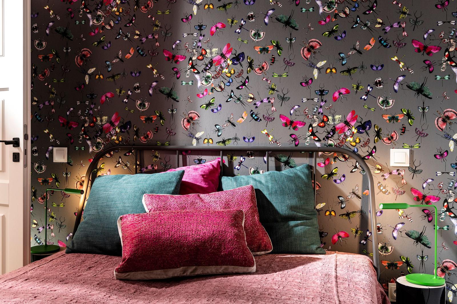 Schlafzimmer mit Bett und buntem Schmetterlings-Muster an den Wänden.
