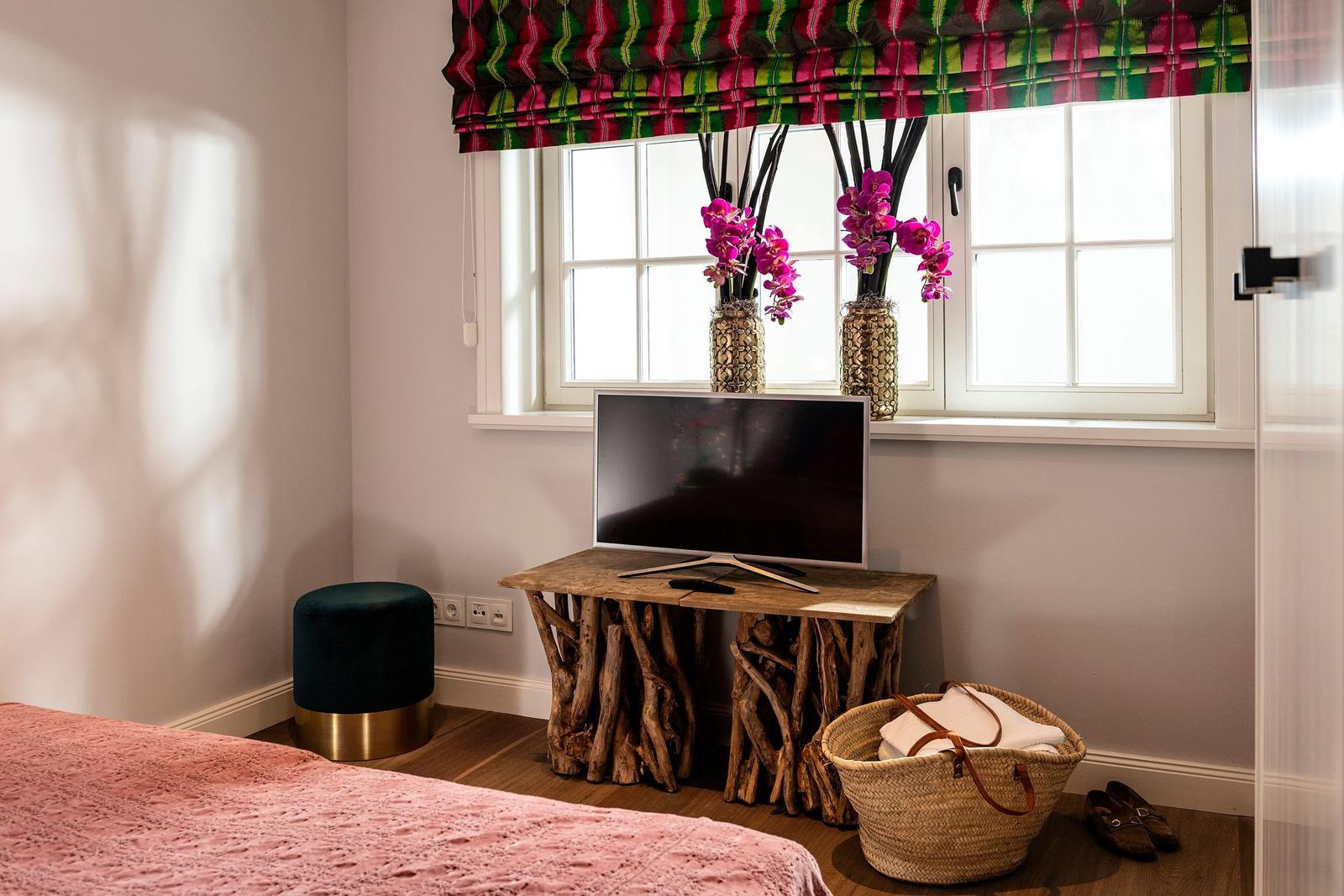 Ein Zimmer mit Bett, TV-Tisch aus Baumstämmen, Blumen und Fenster