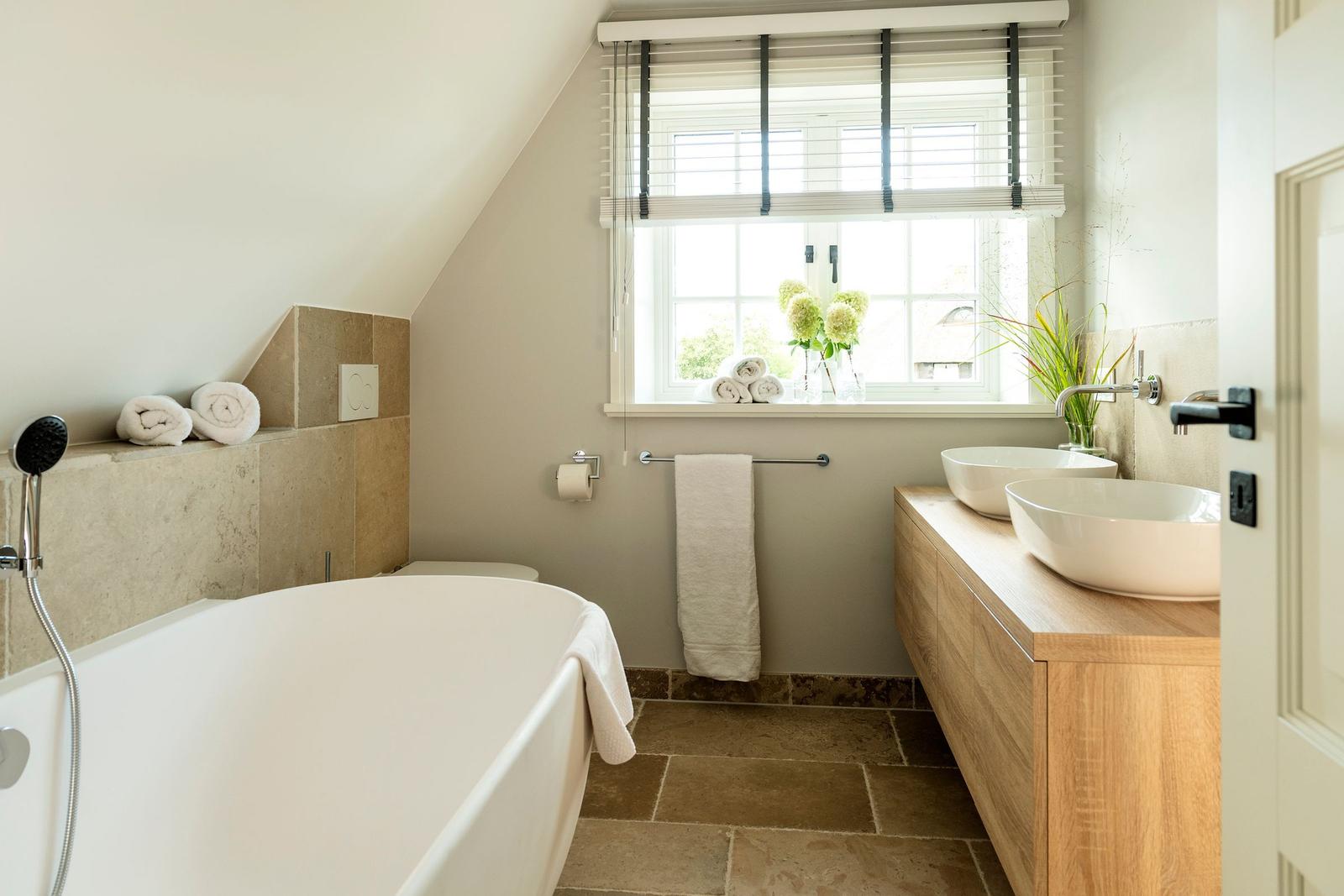 Bad mit Badewanne, Doppelwaschbecken und Fenster mit Blumen.