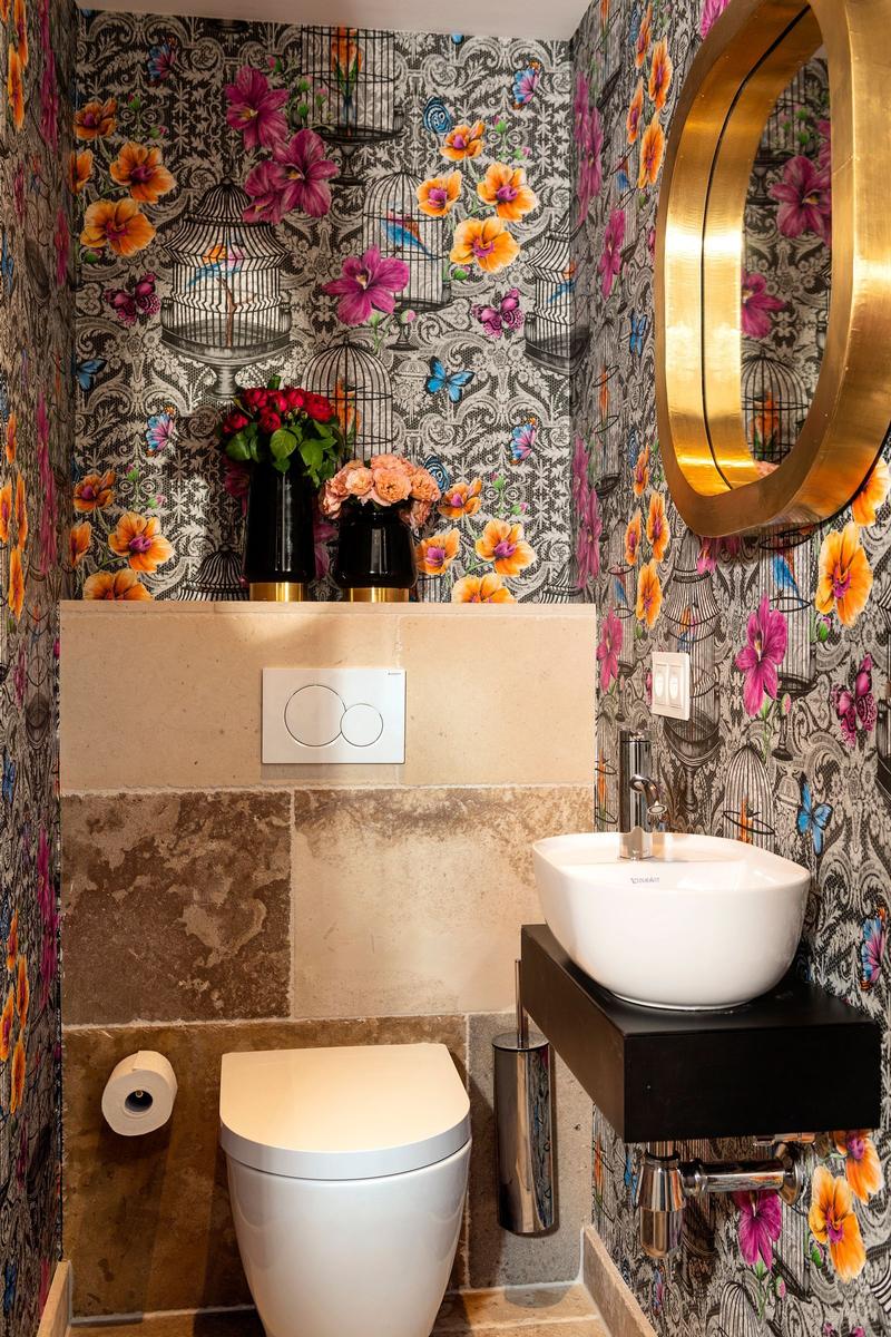 Badezimmer mit floraler Tapete, Waschbecken und Toilette.