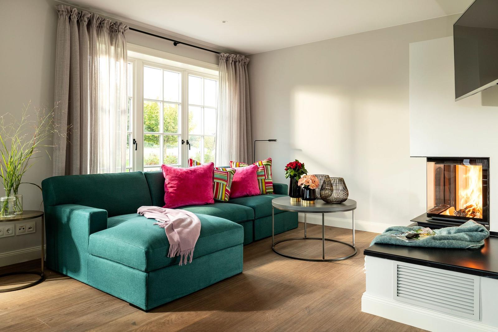Ein Wohnzimmer mit grünem Sofa, Kamin und großem Fenster.
