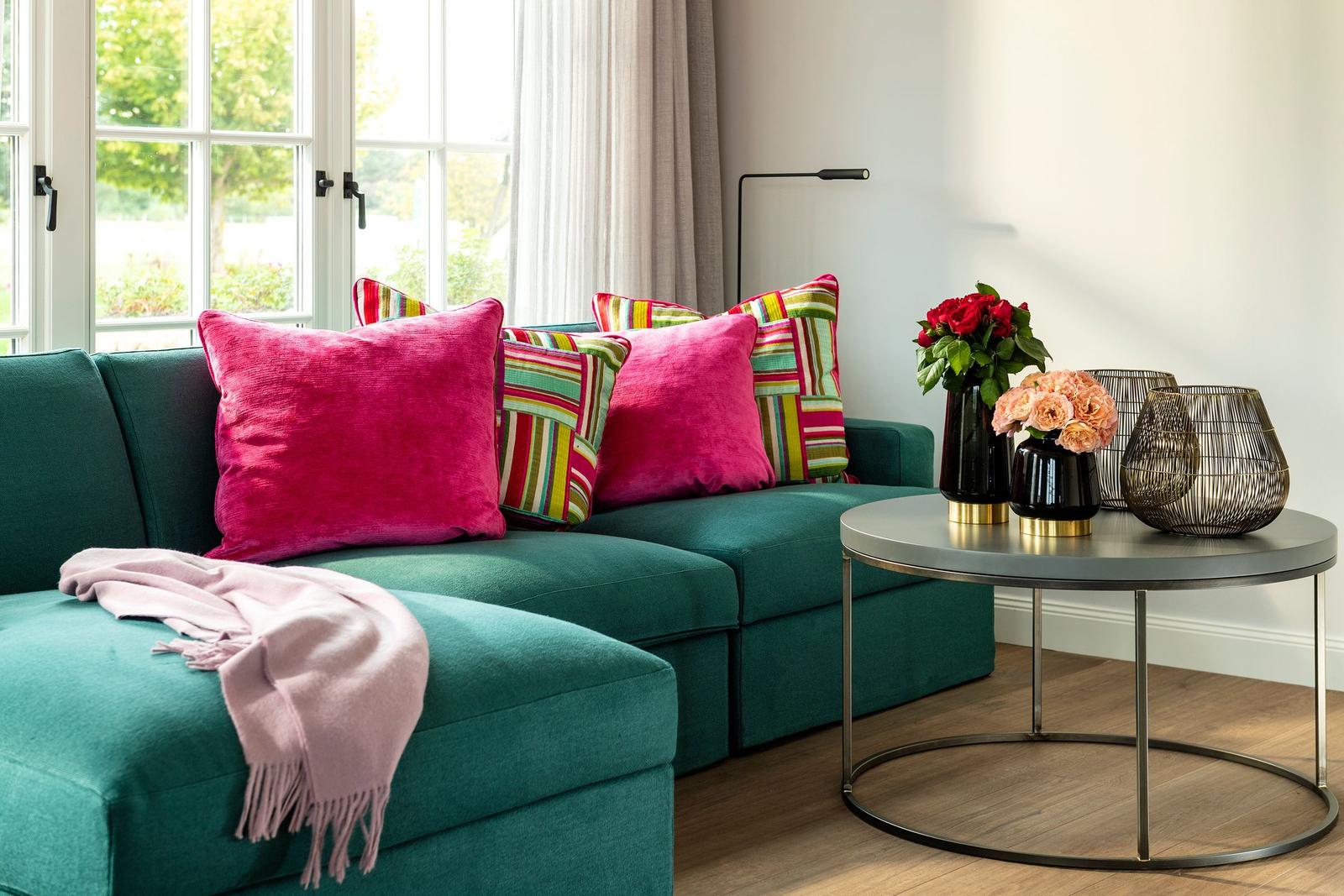 Ein grünes Sofa mit Kissen und einem Beistelltisch mit Blumen.