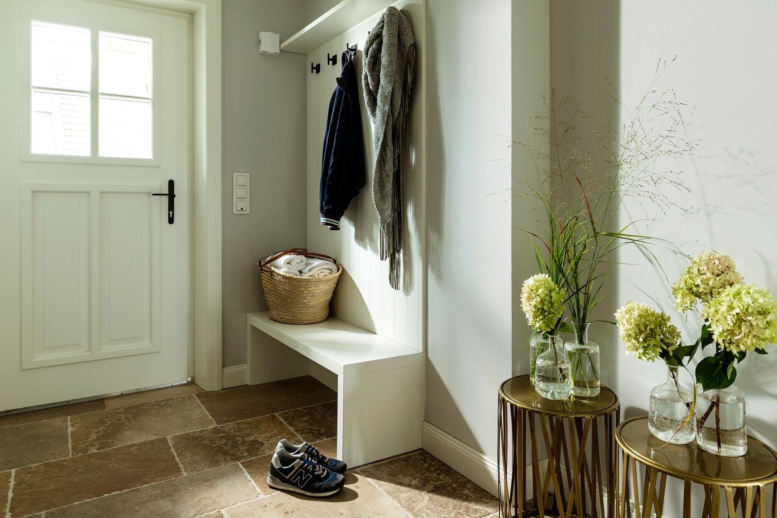Eingangsbereich mit Schuhen, Bänke, Blumen und Kleidung an Haken.