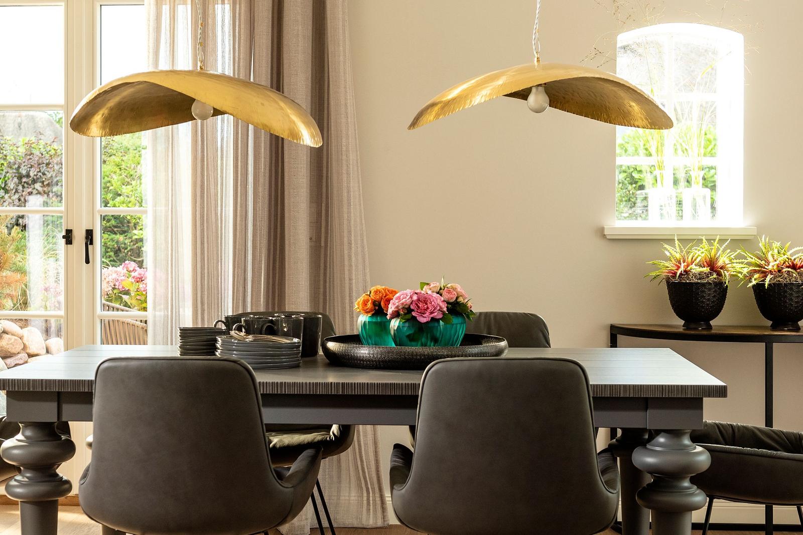 Esstisch mit Stühlen, goldenen Lampen und Blumenarrangement