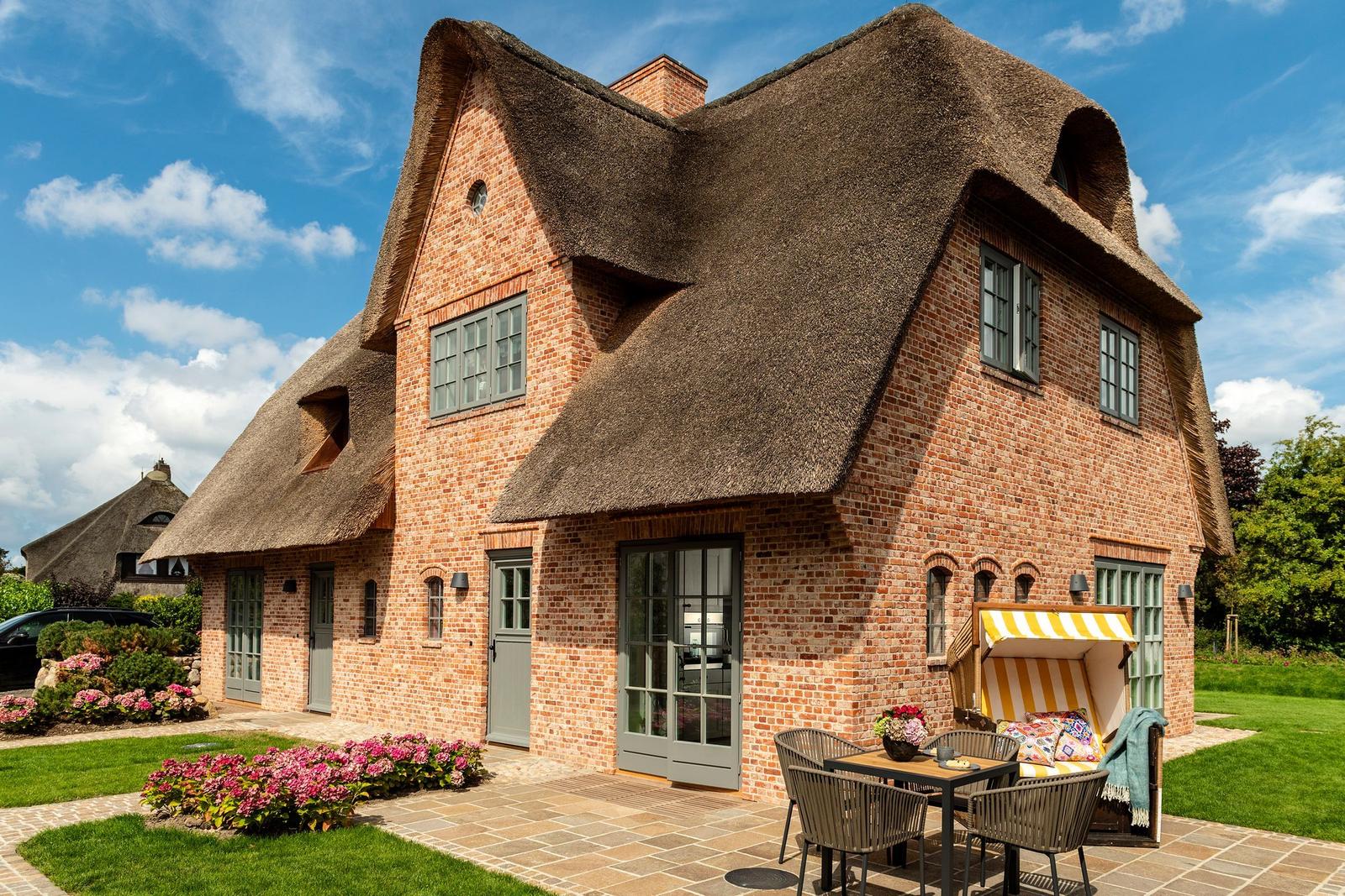 Haus mit Strohdach, Terrasse und Garten. Außentisch mit Stühlen und Sonnenschutz.