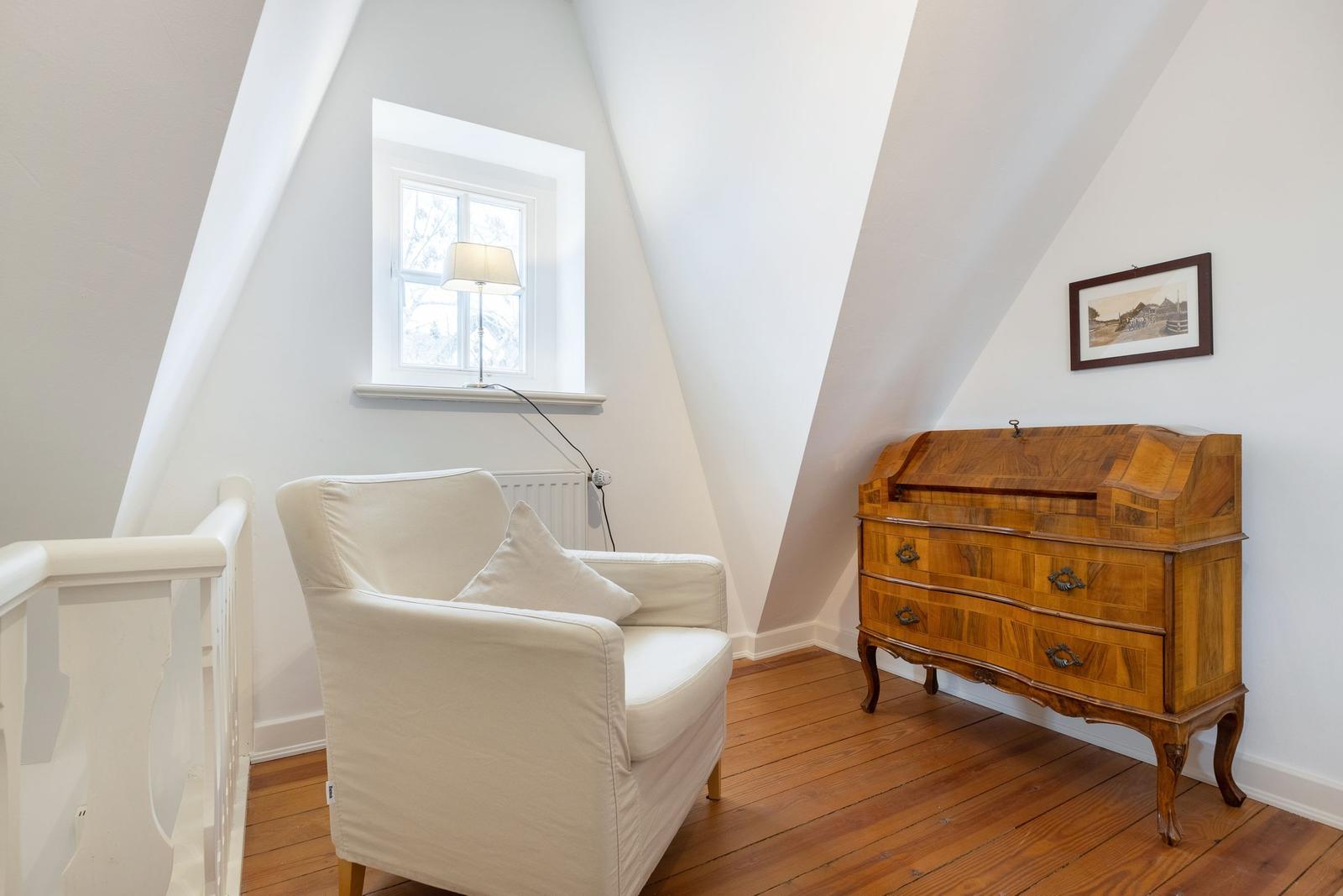Dachzimmer mit Sessel, Holzschrank und Fenster