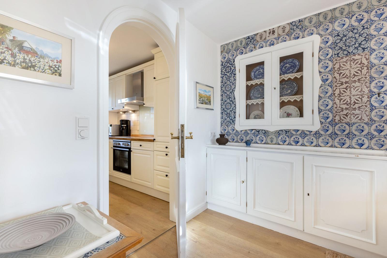 Küche mit weißer Einbauküche und Holzboden. Wand mit blau-weißen Fliesen und Schrank.
