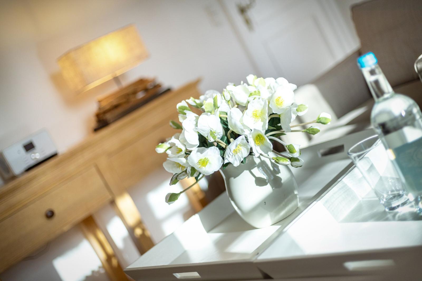 Weißer Blumenstrauß in Vase auf Tisch neben Wasserflasche und Glas.