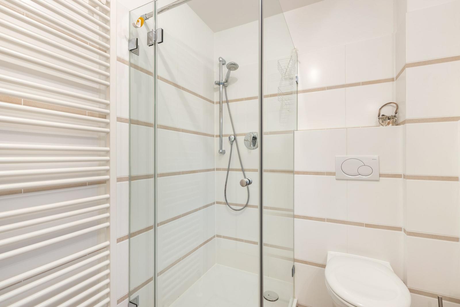 Bad mit Dusche, Toilette und Heizung. Fliesen mit beige Streifen.