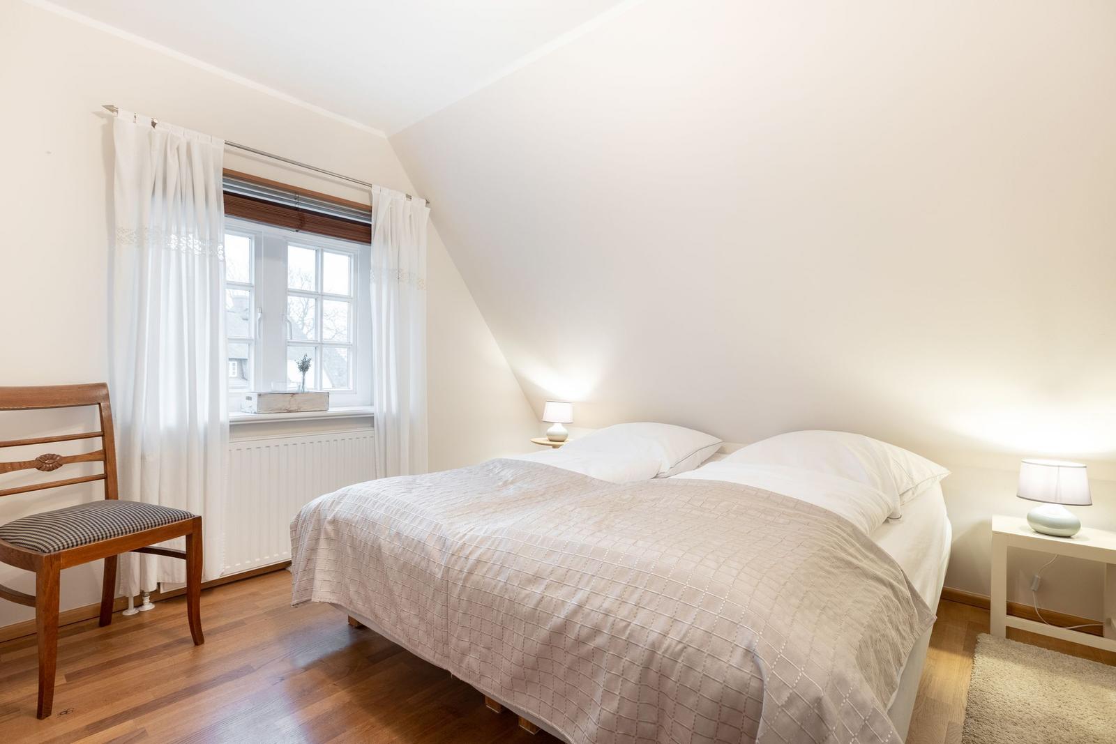 Schlafzimmer mit Dachbodenfenster, Bett, Nachttisch und Holzstuhl.