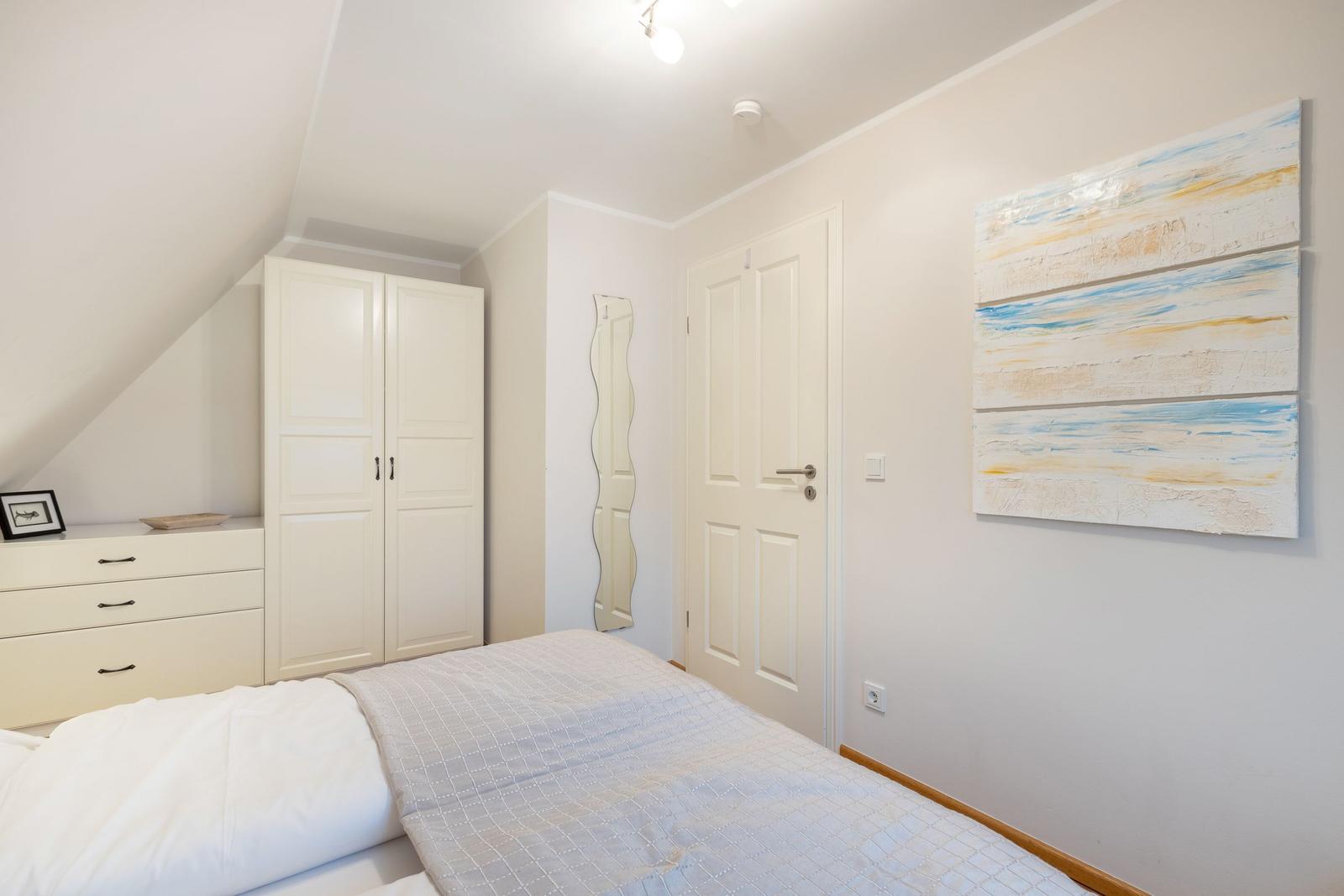 Schlafzimmer mit Bett, Kleiderschrank und Wandbild.