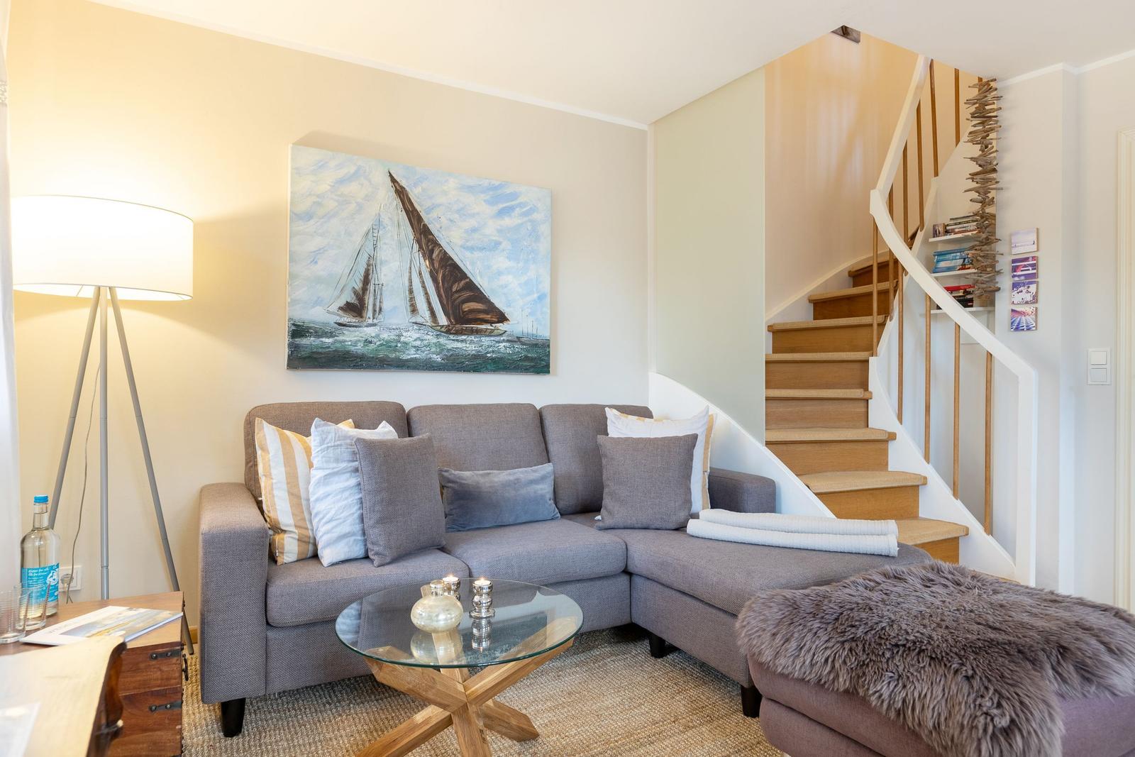 Wohnzimmer mit Sofa, Glas-Tisch und Treppe zur oberen Etage.