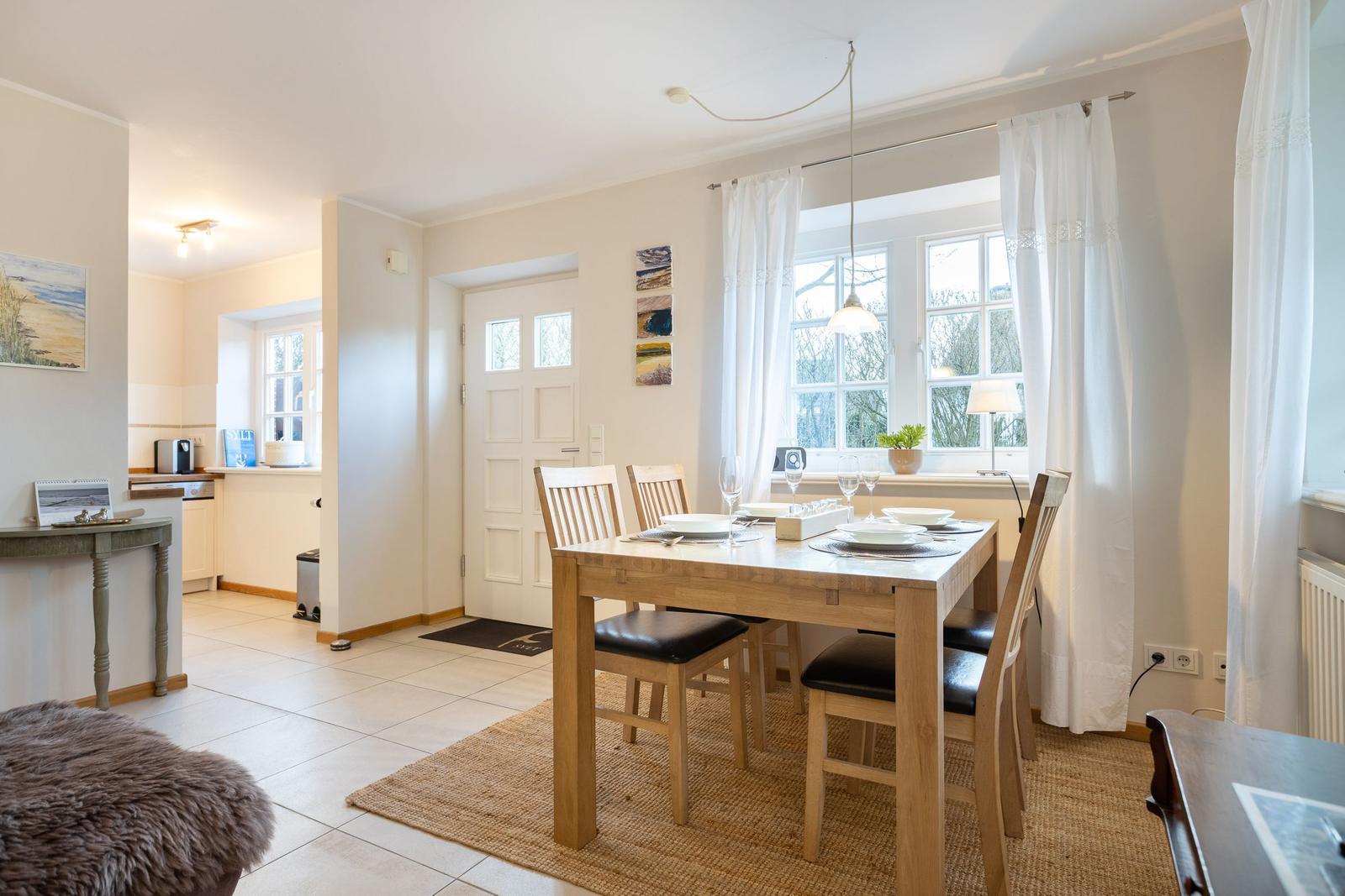 Esszimmer mit Holztisch, Stühlen und Fenster. Küche im Hintergrund.