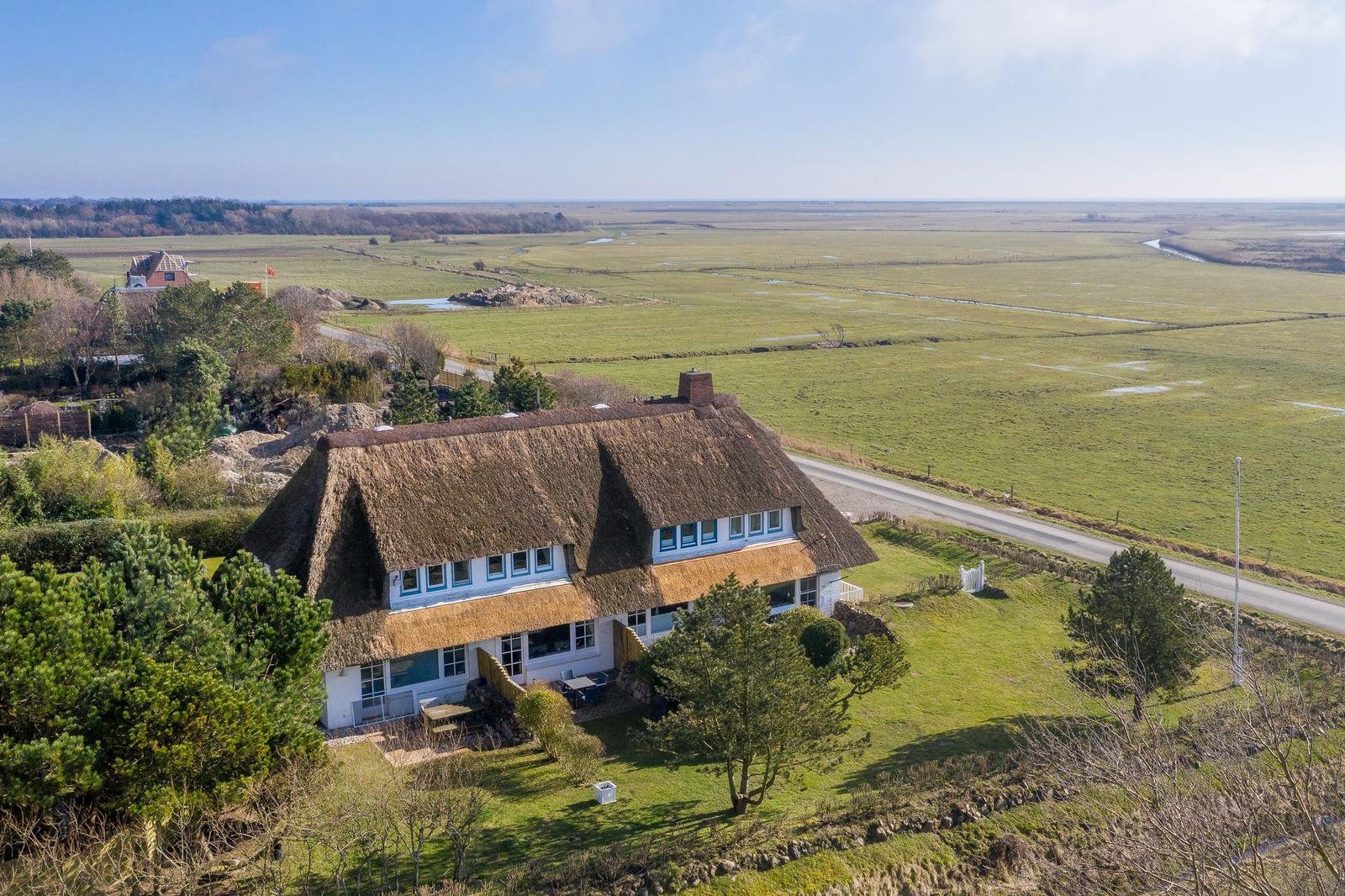 Haus mit Strohdach und Garten. Blick auf grüne Landschaft und Straße.