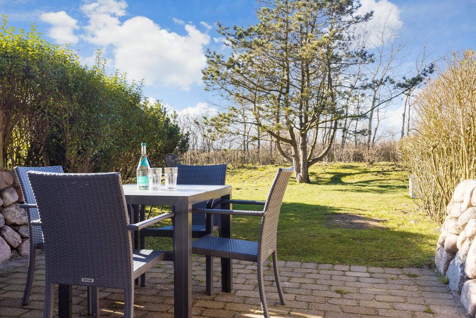 Terrasse mit Tisch und Stühlen, Grasfläche und Bäume im Hintergrund.