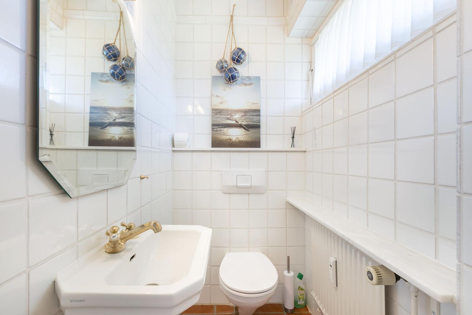 Badezimmer mit Waschbecken, Toilette und Spiegel an weißen Fliesenwänden.