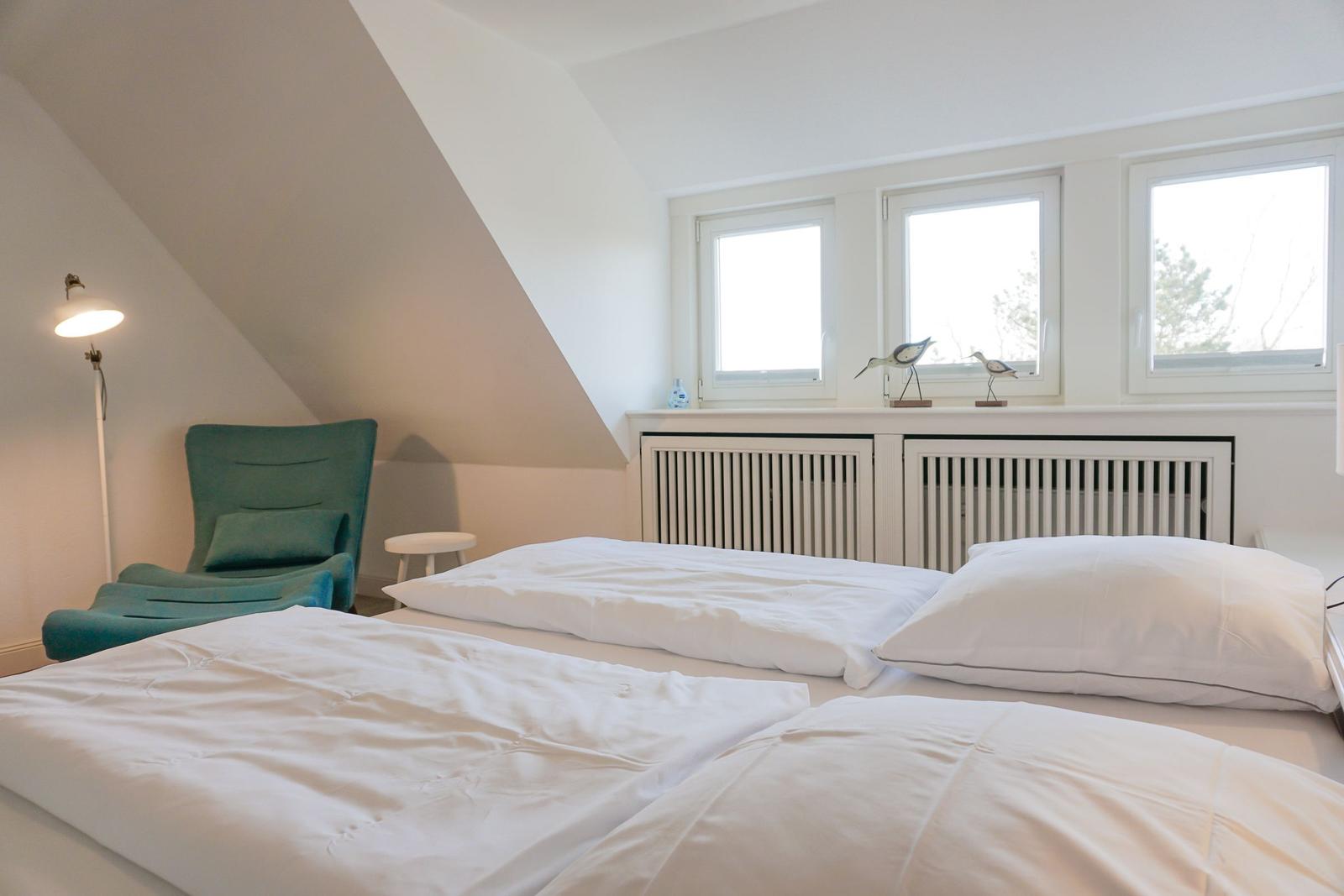 Schlafzimmer mit Doppelbett, grüner Sessel und Fenstern.