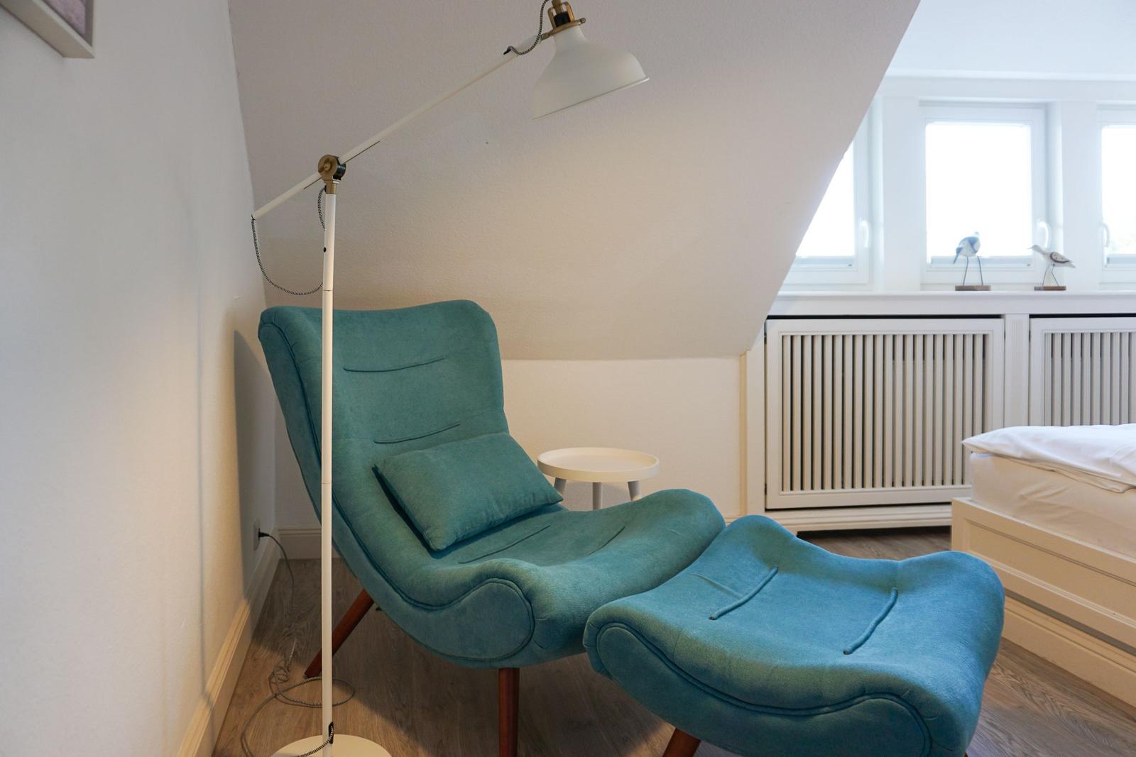Blauer Sessel mit Fußstütze neben Bett und Fenster