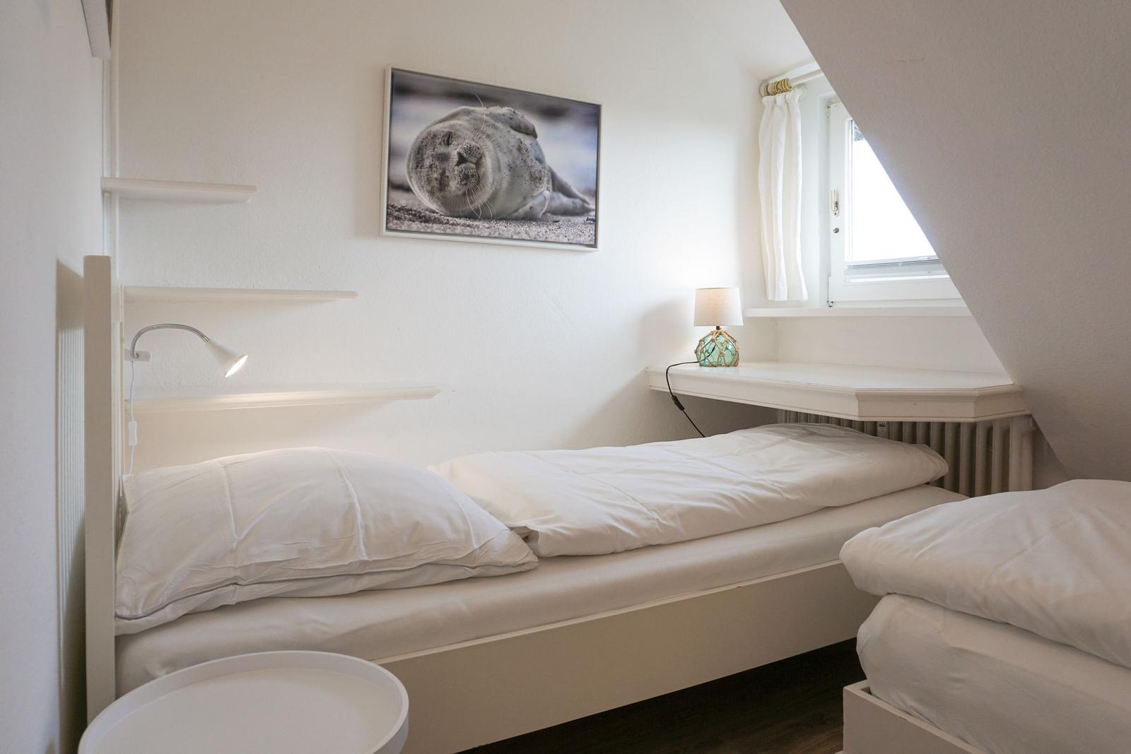 Zimmer mit zwei Betten, Wandbild und Fenster unter Dachschräge.
