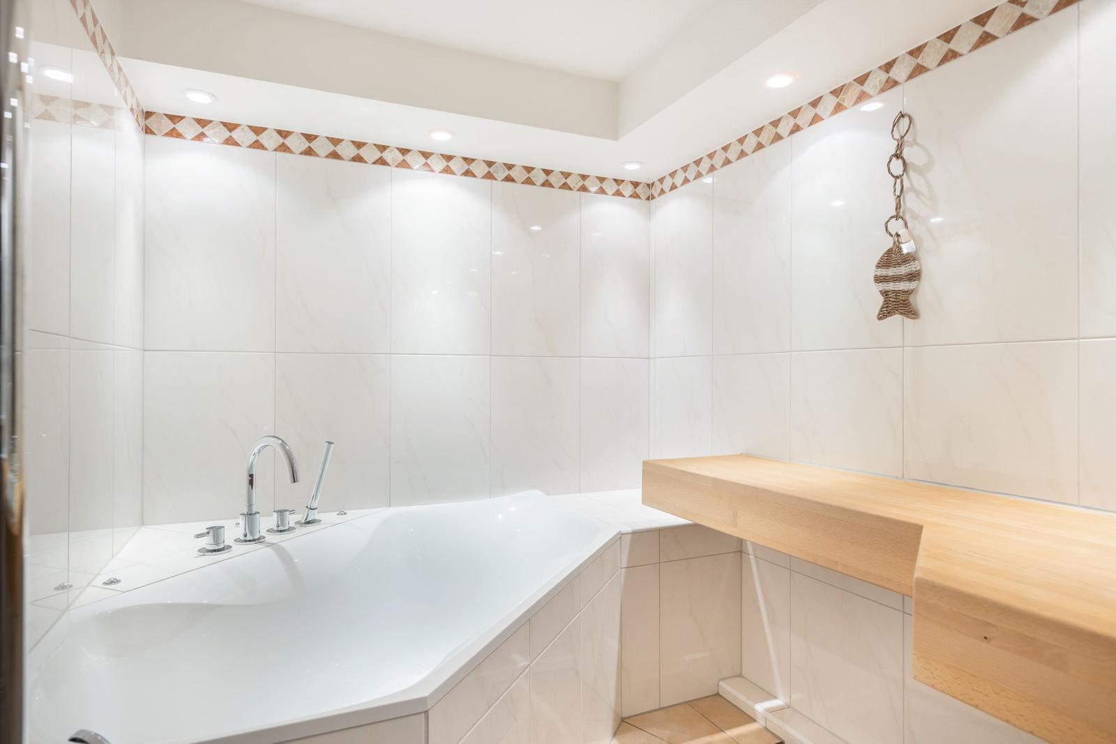 Badezimmer mit Badewanne, Holzbank und Wandfliesen mit Muster.