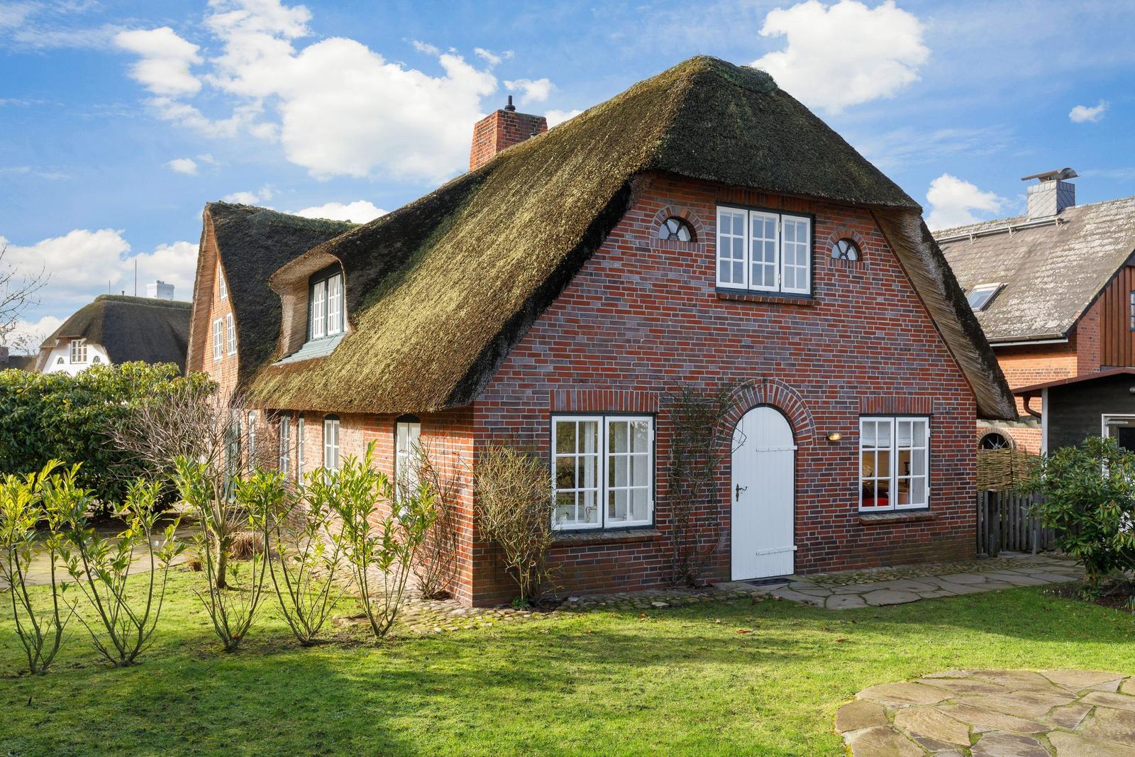 Red brick house with thatched roof and white door.