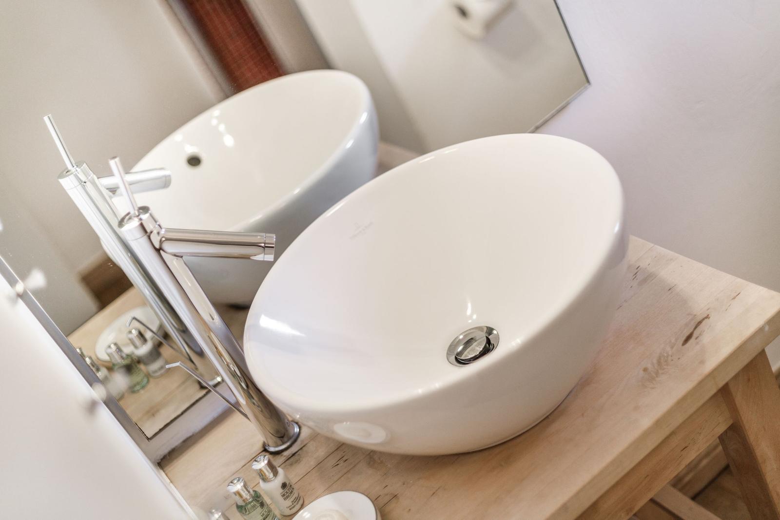 White vessel sink on wooden vanity with modern faucet.