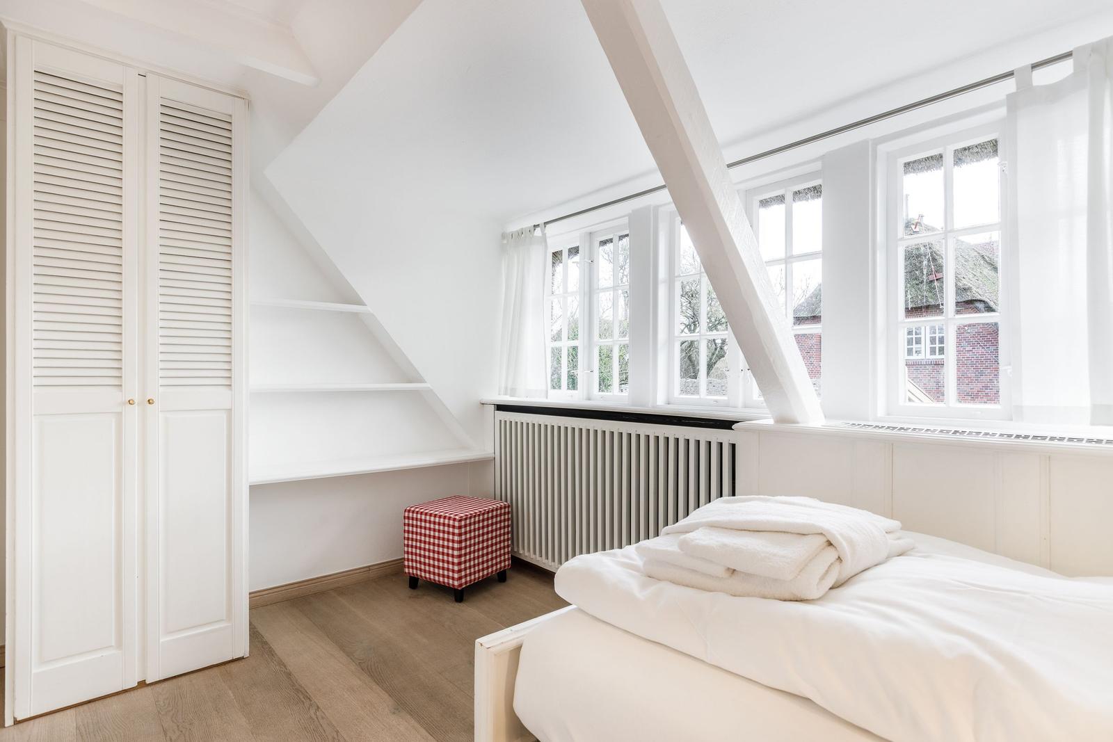 Bedroom with sloped ceiling, windows, and white bed.