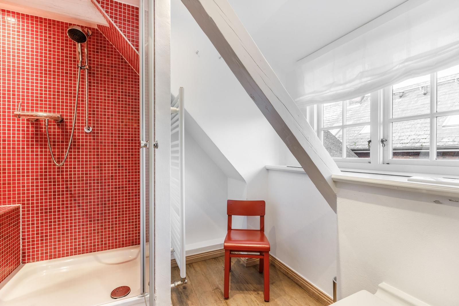 Shower area with red tiles and red chair under sloped roof.