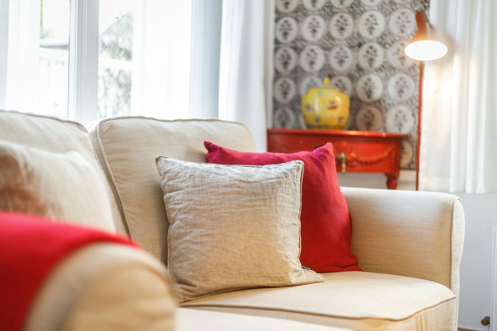A sofa with cushions near a window and a red sideboard.