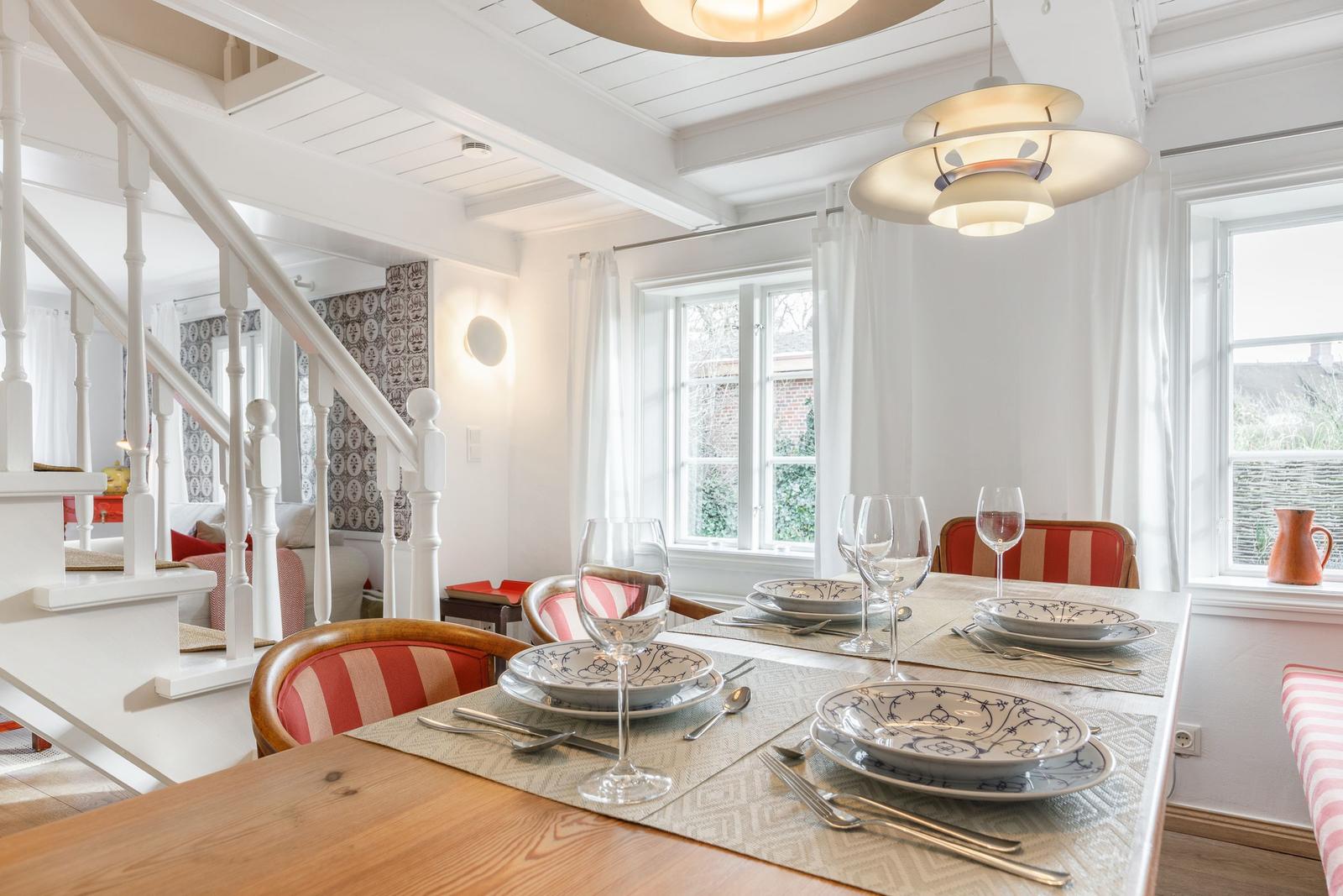 Dining table for four, red chairs, windows with white curtains.