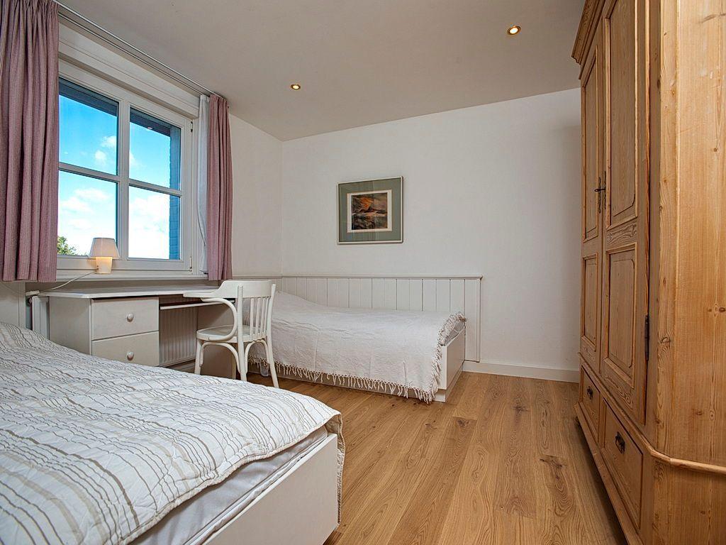 Zimmer mit zwei Betten, Schreibtisch und Holzschrank. Fenster mit Vorhängen und Wandbild.