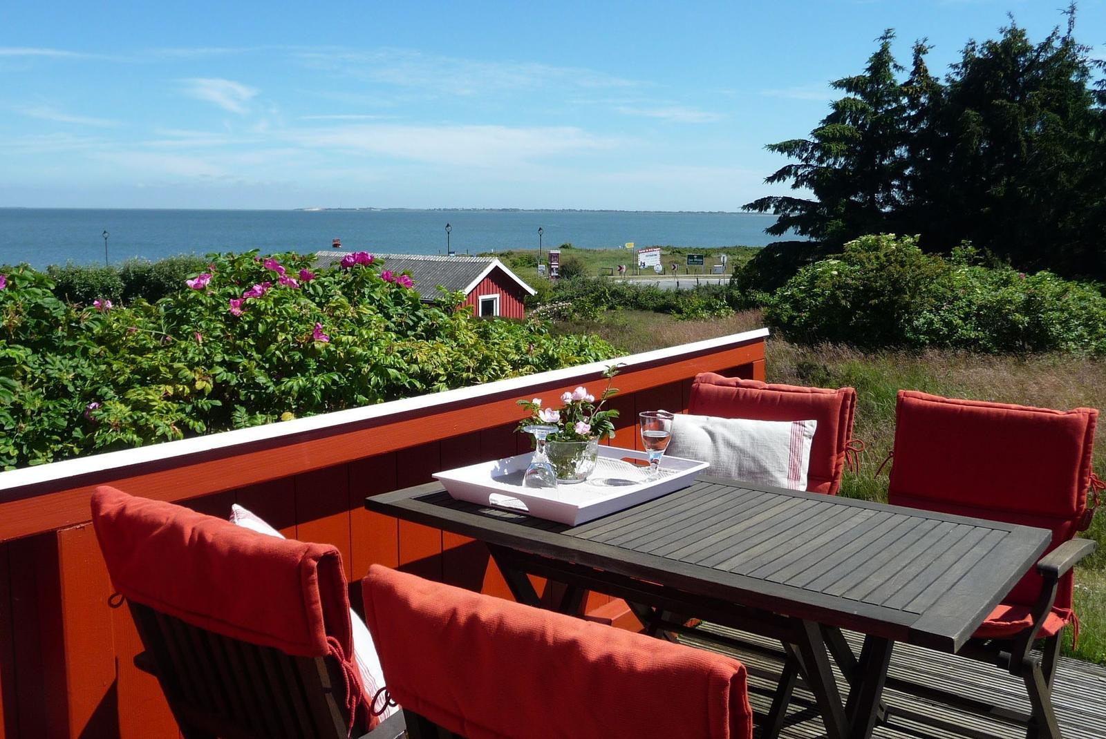 Terrasse mit Tisch und Stühlen, Blick auf Meer und grüne Landschaft.