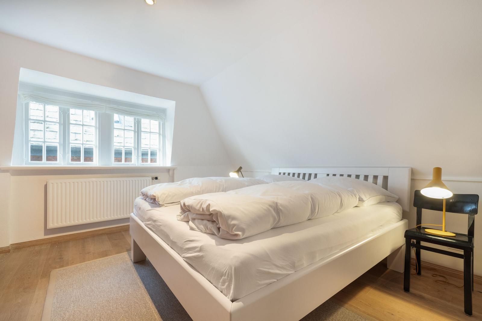 Bedroom with bed, window, and chair with lamp.