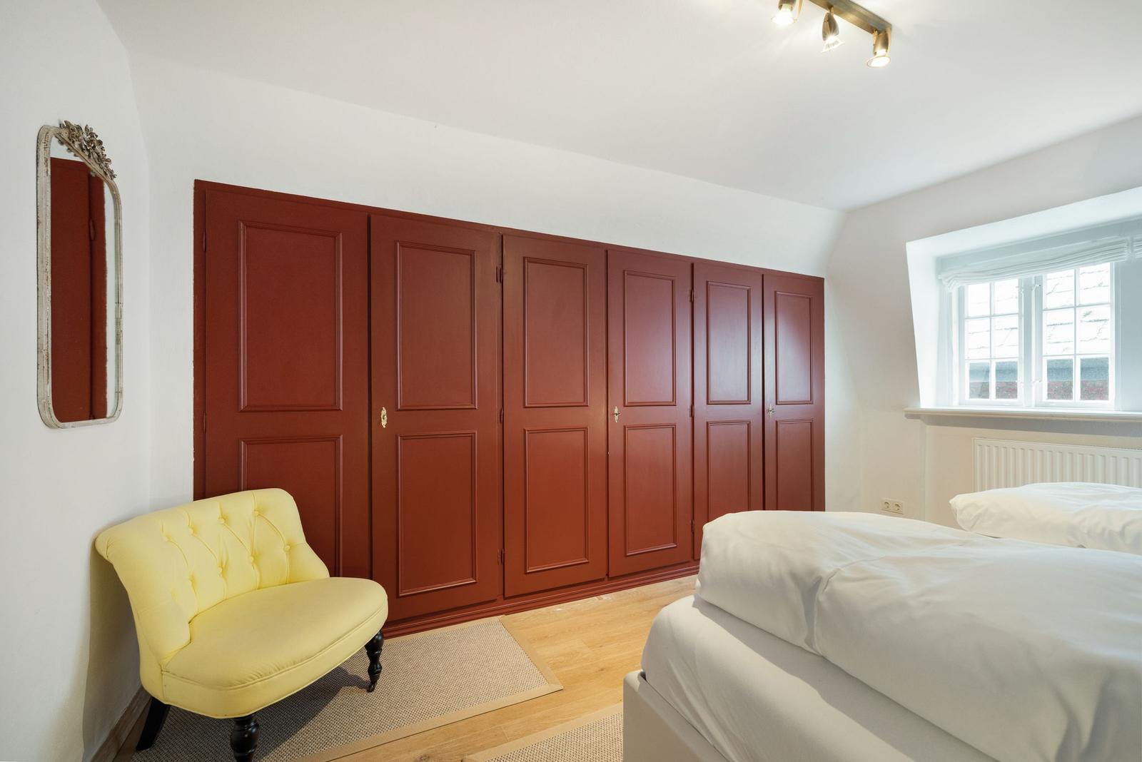 Bedroom with bed, yellow seating, and red wardrobe.