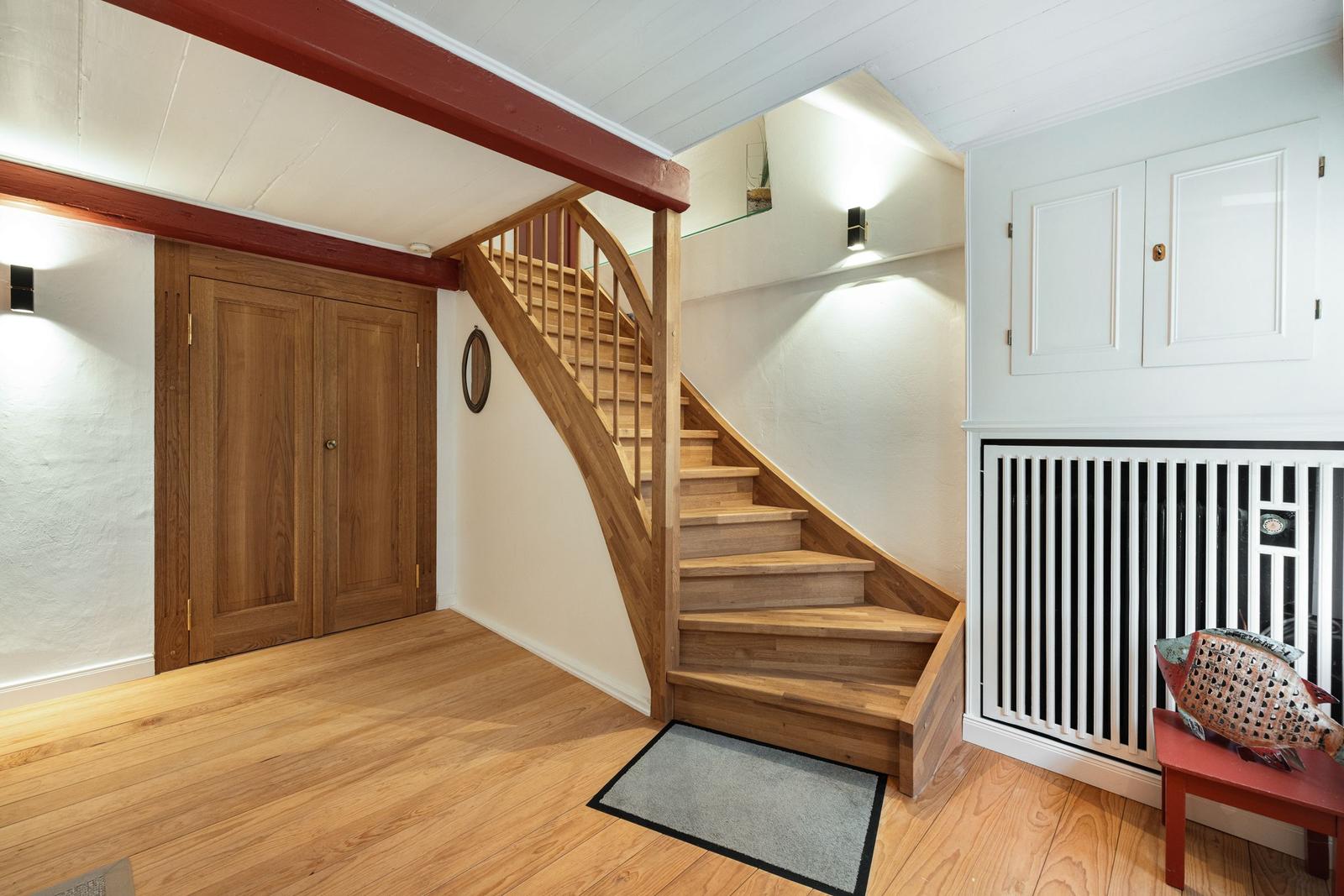 Wooden staircase leads to an upper level. Wooden floor, white walls, and wooden doors.