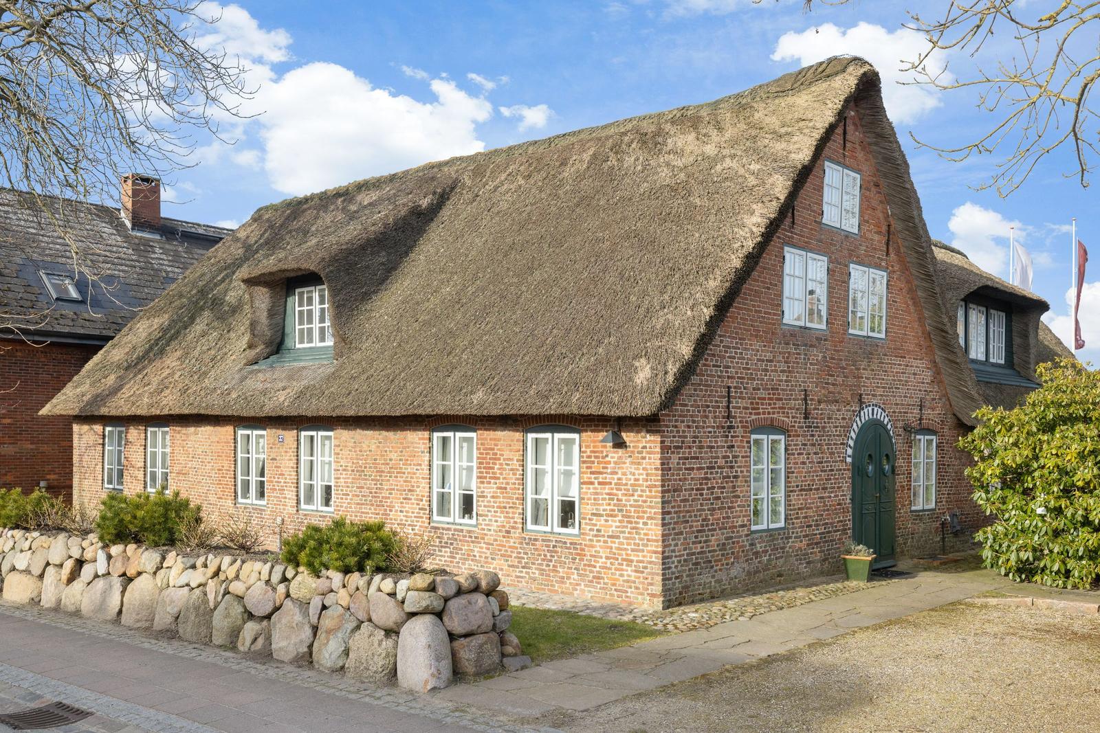 Traditional house with thatched roof and brick facade. Green door and windows.