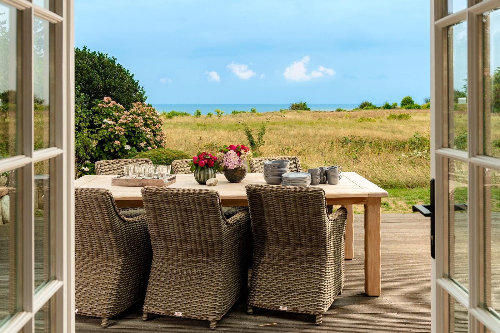Terrasse mit Tisch und Stühlen, Blick auf das Meer und Grasland.