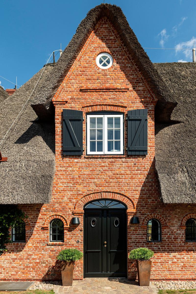 Rotes Backsteinhaus mit Strohdach und schwarzer Tür