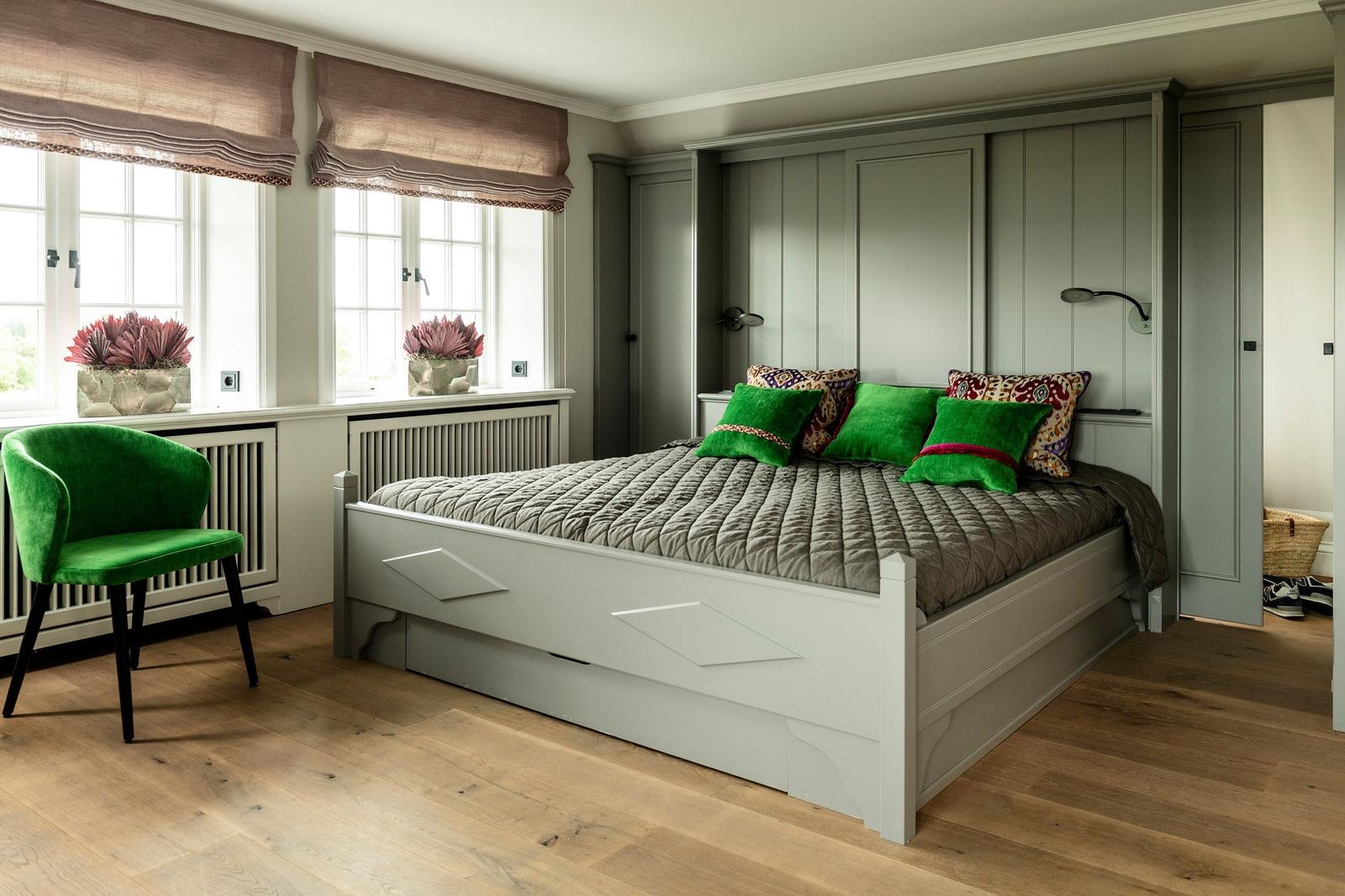 Schlafzimmer mit weißem Bett, grüner Sessel und Holzboden. An der Wand sind Schiebetüren.