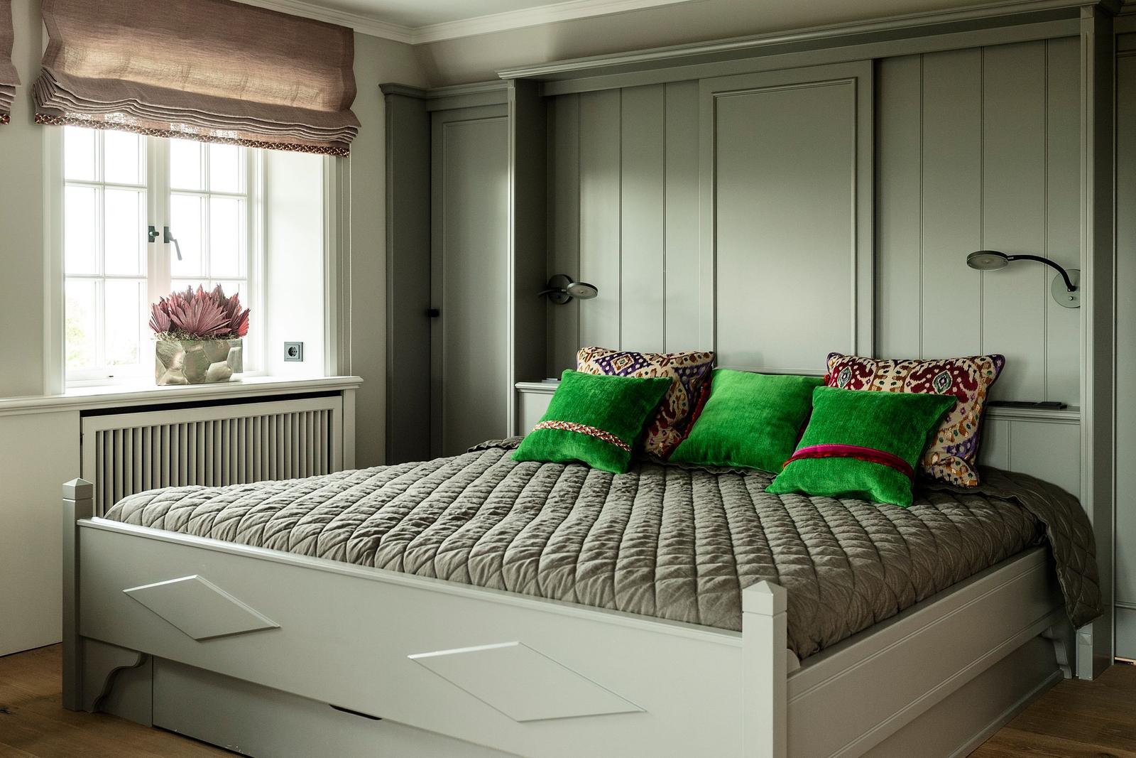 Schlafzimmer mit Bett, grünen Kissen und Fenster mit Vorhang.