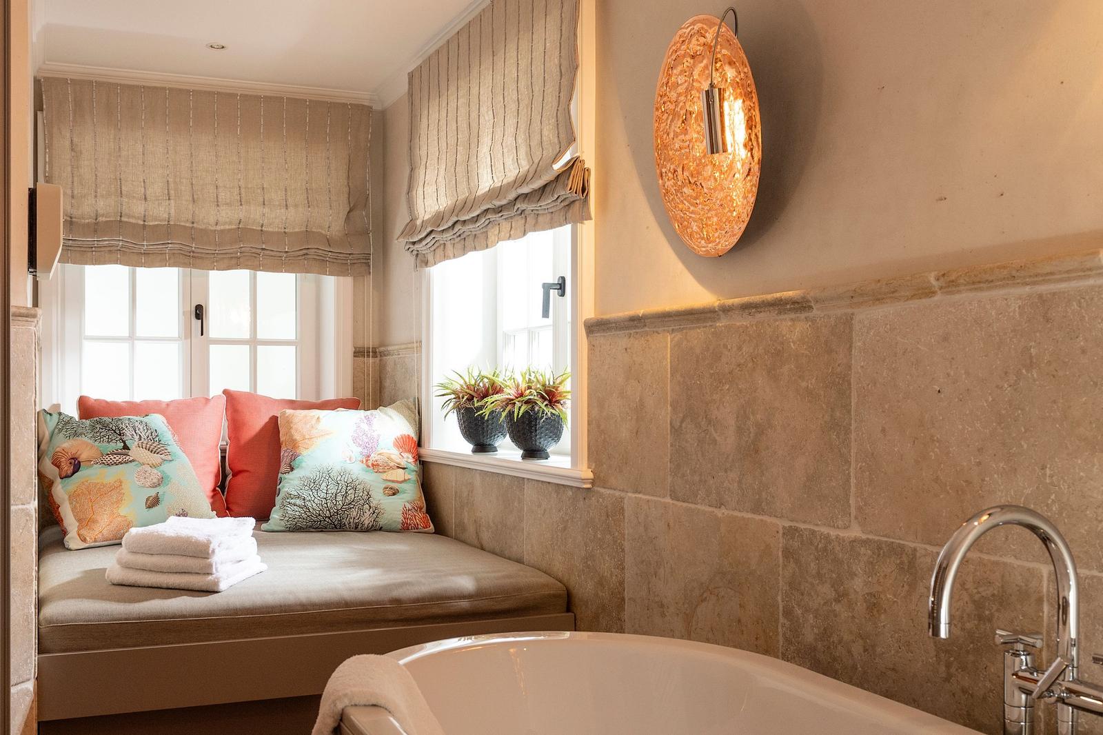 Bad mit Badewanne, Sitzbank, Fenster und Wandbeleuchtung.