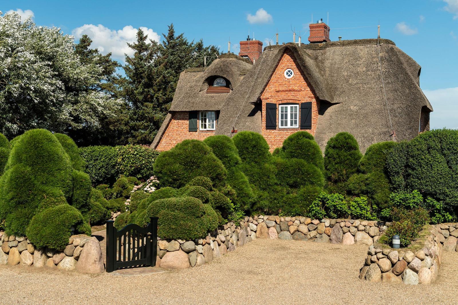 Traditionelles Haus mit Strohdach, umgeben von grünen Hecken und Steinmauern.