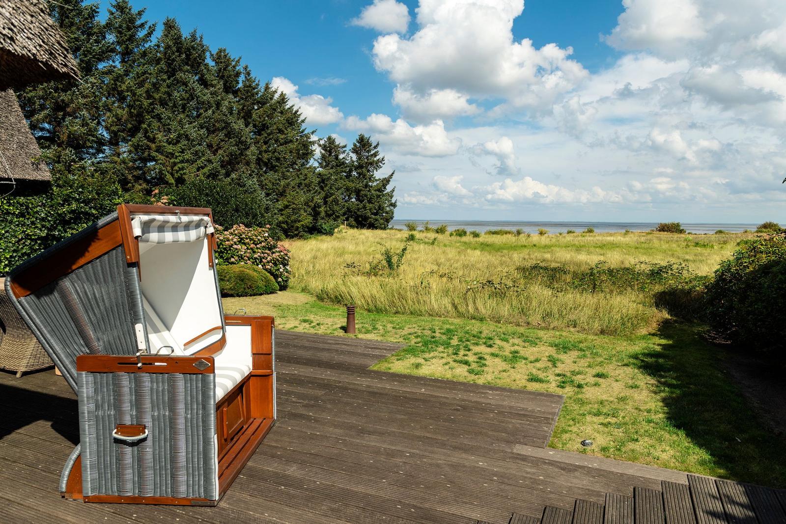 Hochwertiger Strandkorb auf Terrasse mit Blick auf Grasland und Wasser.