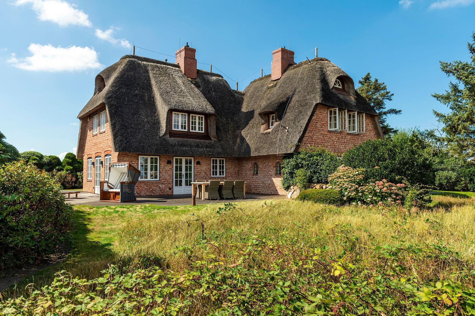 Haus mit Strohdach, Terrasse und Garten im Freien.